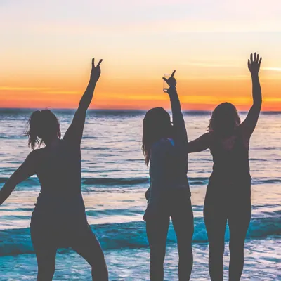 silhouettes of a group of women feeling empowered with their arms raised standing beside the ocean