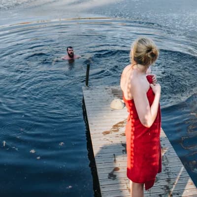 man swimming in the water and woman on the pier deciding whether to join